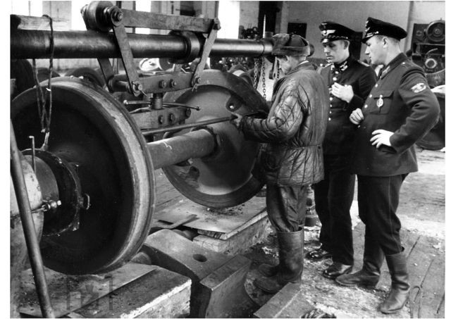 1943   : http://www.eisenbahnstiftung.de
. : Unter den wachsamen Augen zweier Reichsbahner wird die Spurweite einer Achse im Eisenbahn-Ausbesserungswerk (EAW) Dnjepropetrowsk vermessen. (1943) Foto: Walter Hollnagel 